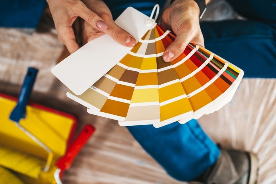 A person holding a fan of yellow and orange wall paint color swatches.