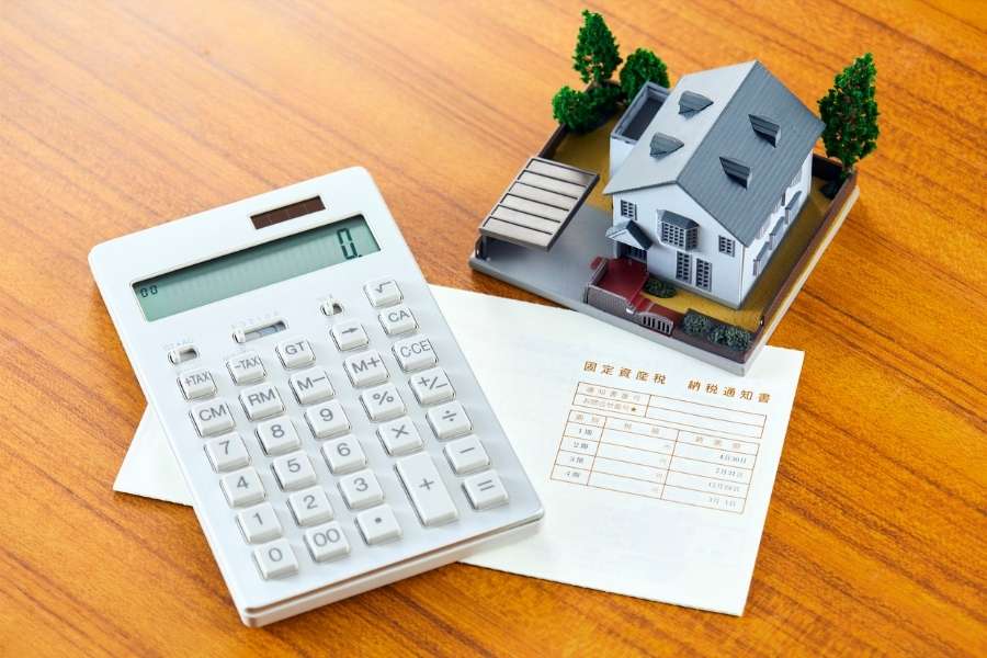 A calculator next to a model house and a tax document, illustrating the process of calculating property taxes.