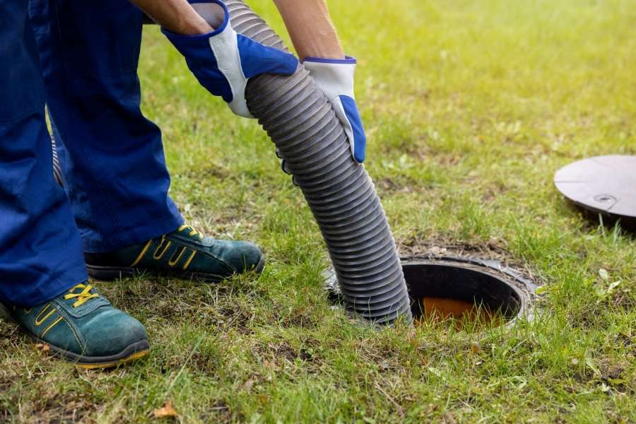 A worker using a vacuum hose to maintain a drainage system clean in a grassy area.