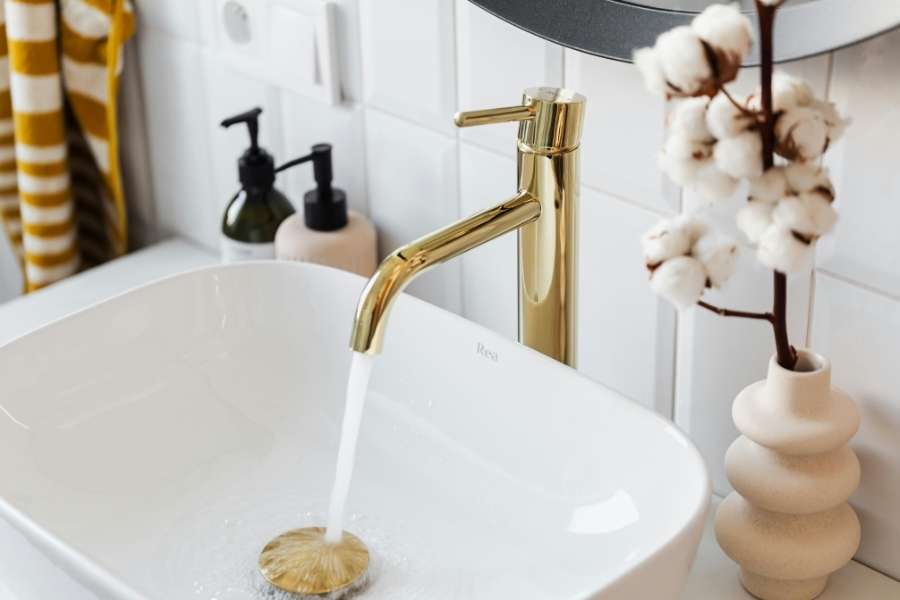 A sleek gold faucet running water into a modern white basin to fix an annoying dripping faucet.